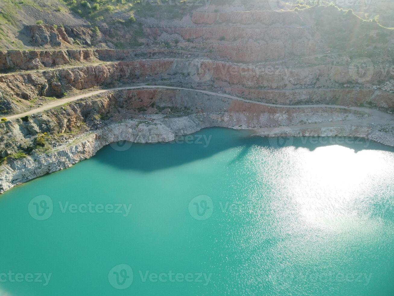 Aerial top view on opencast mining quarry with flooded bottom, turquoise surface of the lake. Quarry pond overgrown with green plants and clear turquoise water photo