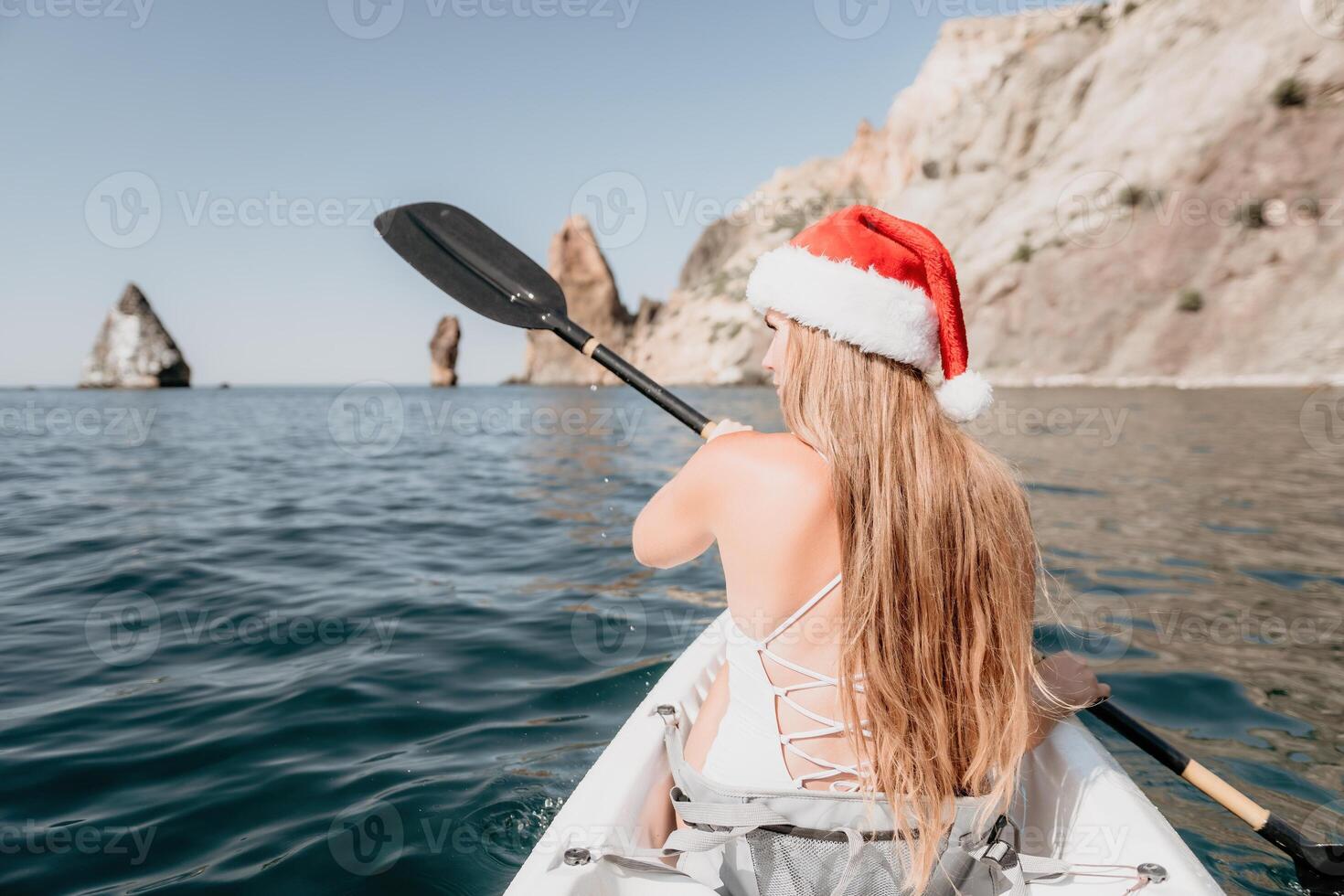 Woman in kayak back view. Happy young woman in Santa hat floating in kayak on calm sea. Summer holiday vacation and cheerful female people relaxing having fun on the boat. photo