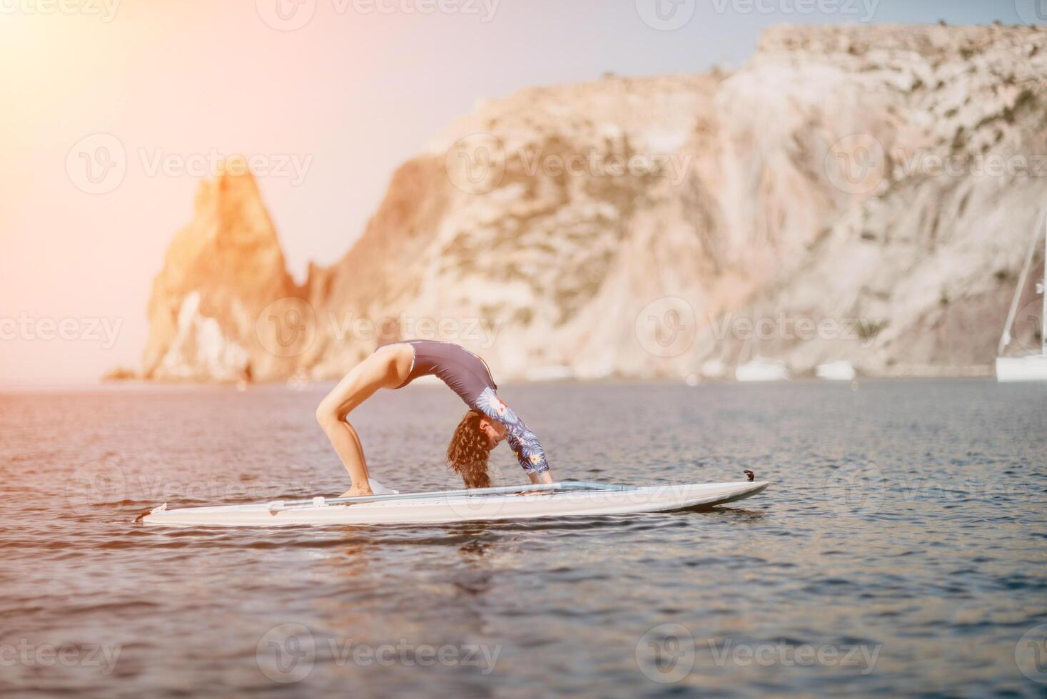 Woman sup yoga. Middle age sporty woman practising yoga pilates on paddle sup surfboard. Female stretching doing workout on sea water. Modern individual female hipster outdoor summer sport activity. photo