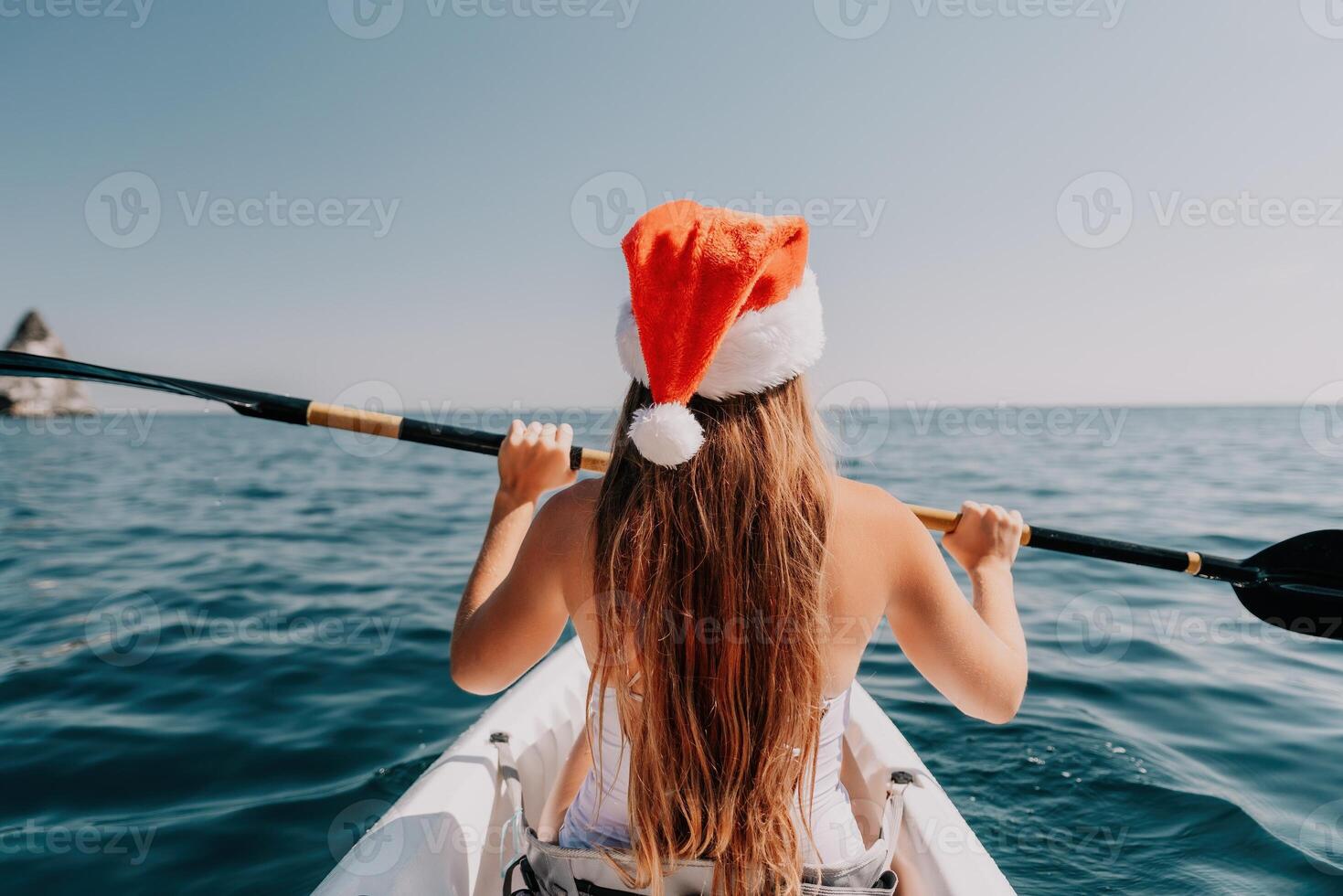 Woman in kayak back view. Happy young woman in Santa hat floating in kayak on calm sea. Summer holiday vacation and cheerful female people relaxing having fun on the boat. photo