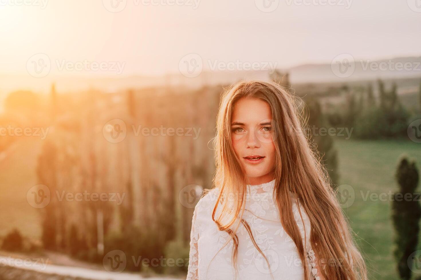 Happy woman in white boho dress on sunset in mountains. Romantic woman with long hair standing with her back on the sunset in nature in summer with open hands. Silhouette. Nature. Sunset. photo