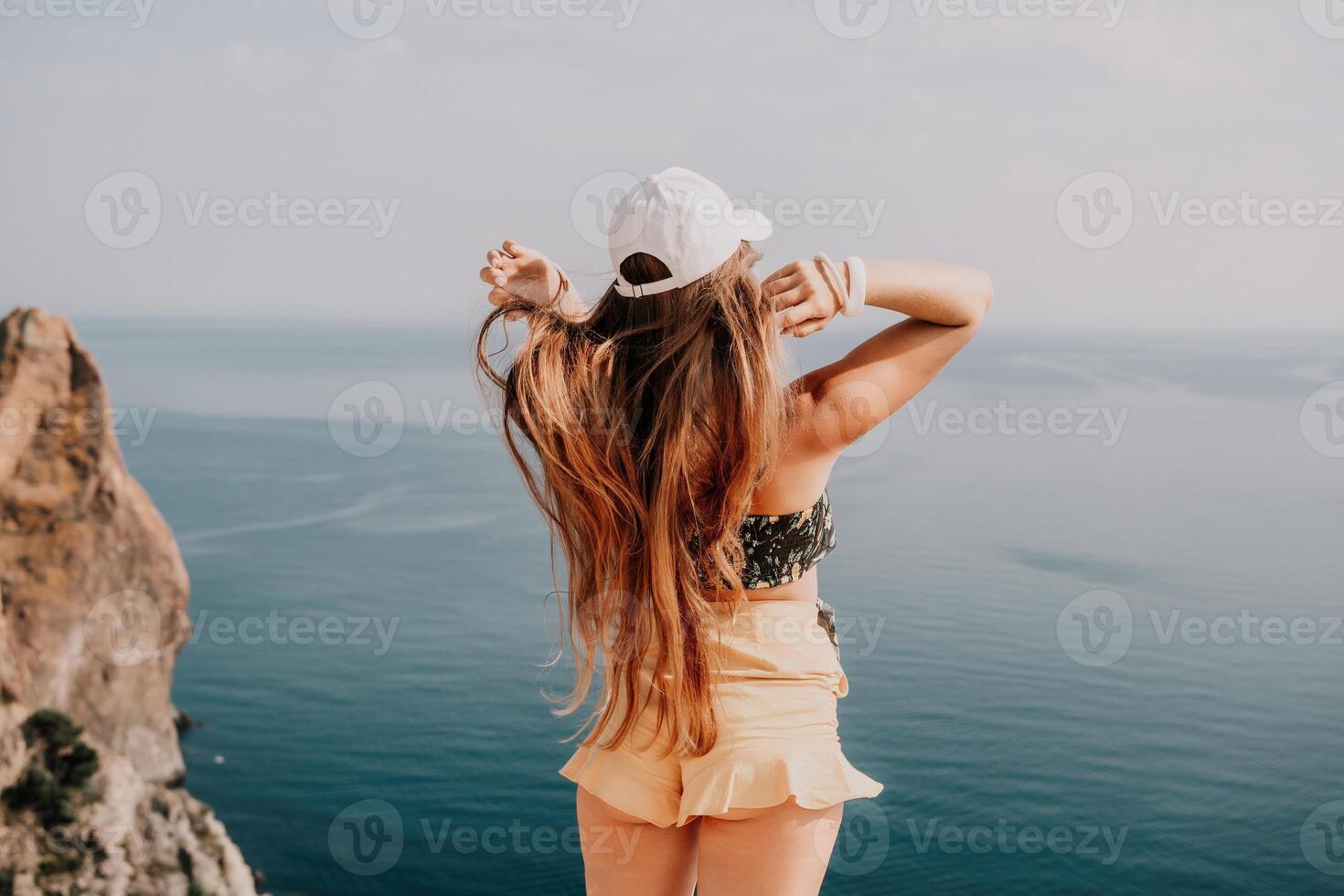 Woman travel sea. Happy tourist enjoy taking picture outdoors for memories. Woman traveler looks at the edge of the cliff on the sea bay of mountains, sharing travel adventure journey photo
