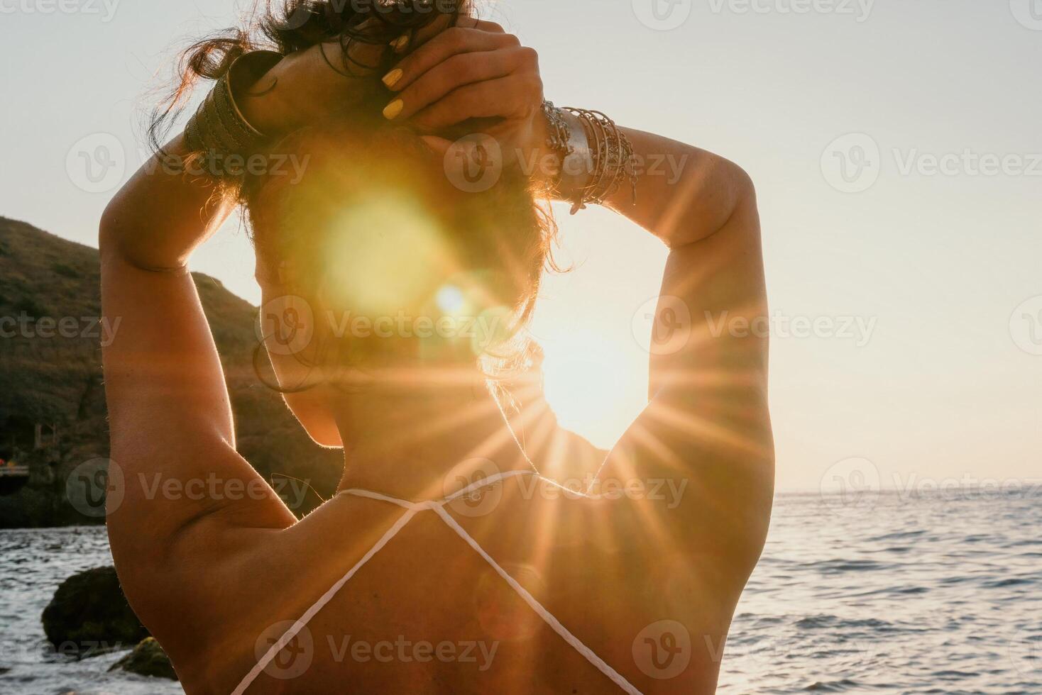 Woman sea yoga. Happy woman in white swimsuit and boho style braclets practicing outdoors on yoga mat by sea on sunset. Women yoga fitness routine. Healthy lifestyle, harmony and meditation photo