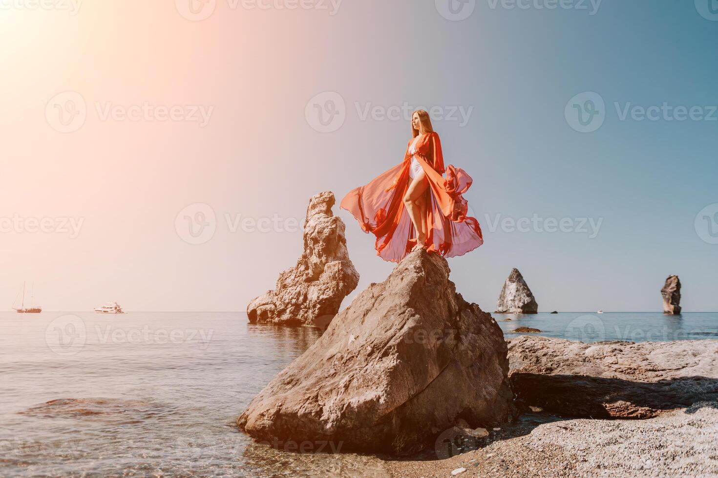 Woman travel sea. Young Happy woman in a long red dress posing on a beach near the sea on background of volcanic rocks, like in Iceland, sharing travel adventure journey photo