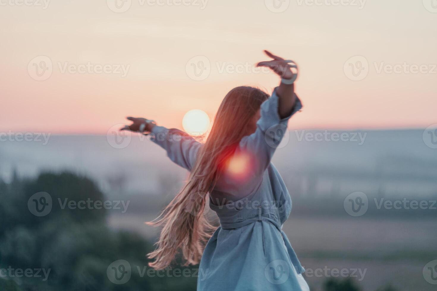 Happy woman standing with her back on the sunset in nature in summer with open hands. Romantic beautiful bride in white boho dress posing with mountains on sunset photo