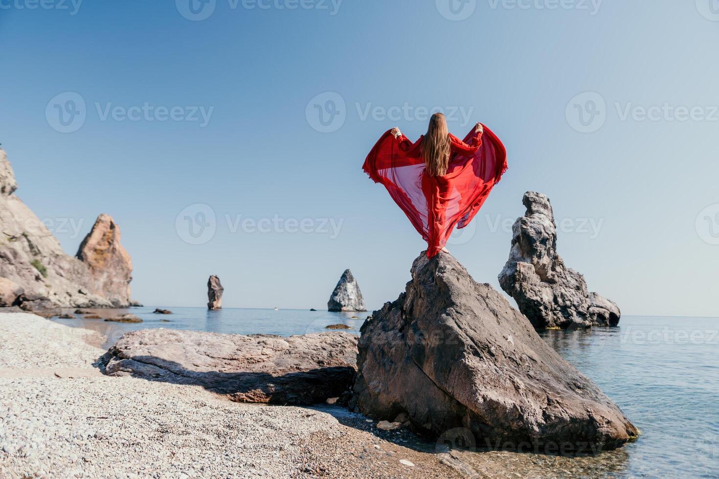 Woman travel sea. Young Happy woman in a long red dress posing on a beach near the sea on background of volcanic rocks, like in Iceland, sharing travel adventure journey photo