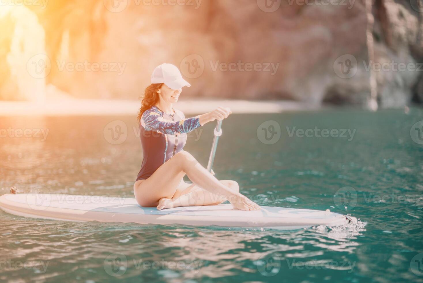 Woman sup yoga. Middle age sporty woman practising yoga pilates on paddle sup surfboard. Female stretching doing workout on sea water. Modern individual female hipster outdoor summer sport activity. photo