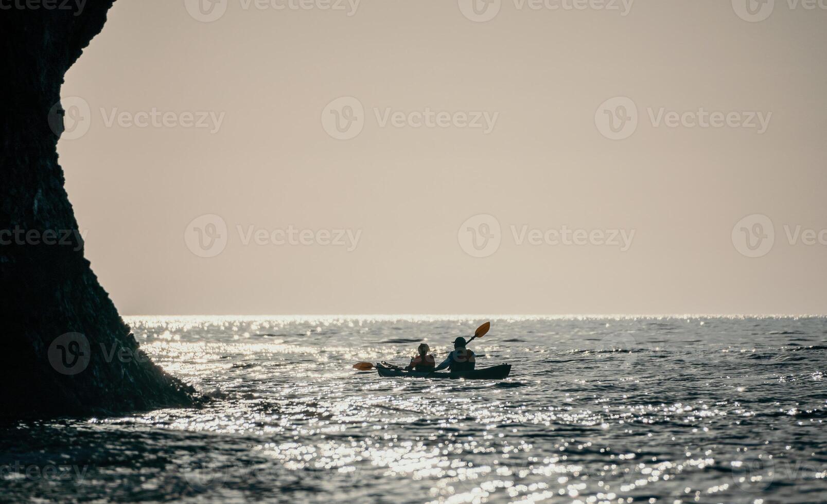 Happy couple kayaks in an inflatable kayak on the sea at sunset. Couple kanoeing in the sea near the island with mountains. People kayaking in life jackets sail. Back view photo