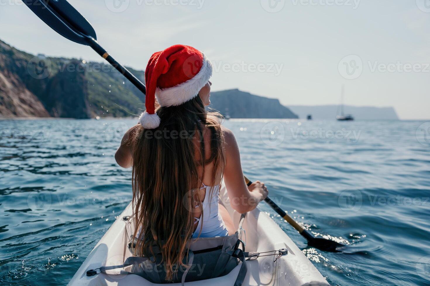 Woman in kayak back view. Happy young woman in Santa hat floating in kayak on calm sea. Summer holiday vacation and cheerful female people relaxing having fun on the boat. photo