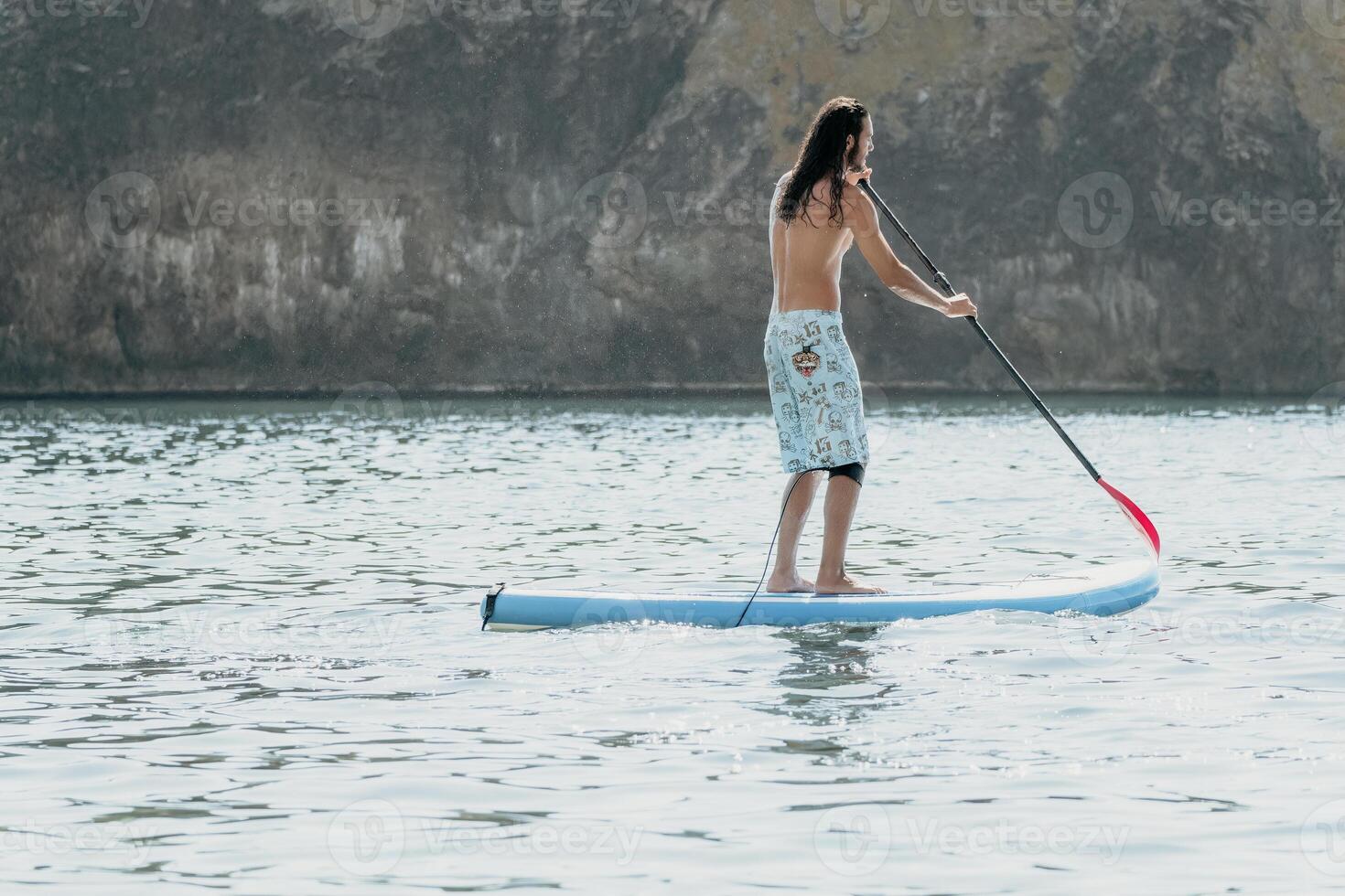 Man Sup Sea. Strong athletic man learns to paddle sup standing on board in open sea ocean on sunny day. Summer holiday vacation and travel concept. Aerial view. Slow motion photo