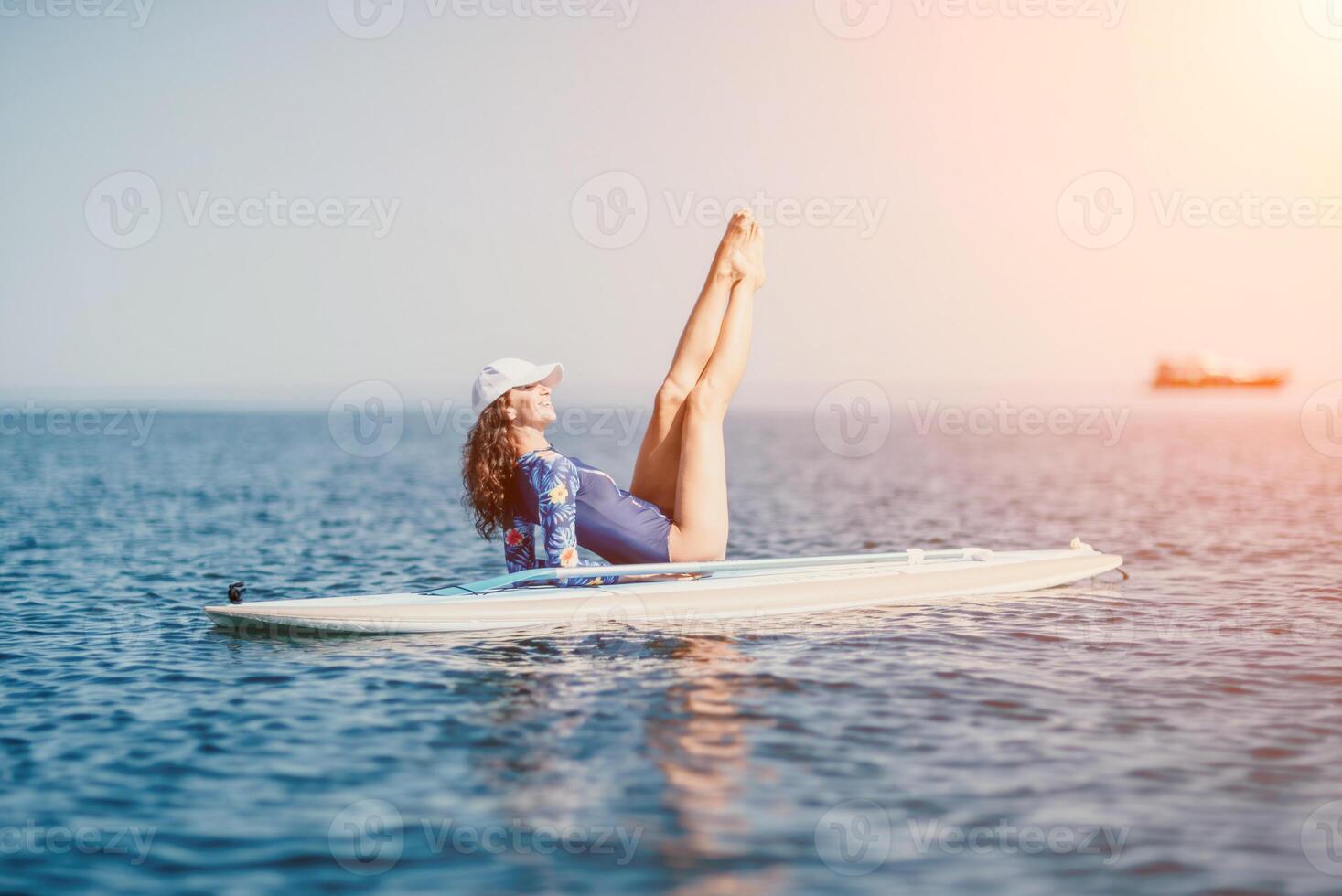 Woman sup yoga. Middle age sporty woman practising yoga pilates on paddle sup surfboard. Female stretching doing workout on sea water. Modern individual female hipster outdoor summer sport activity. photo