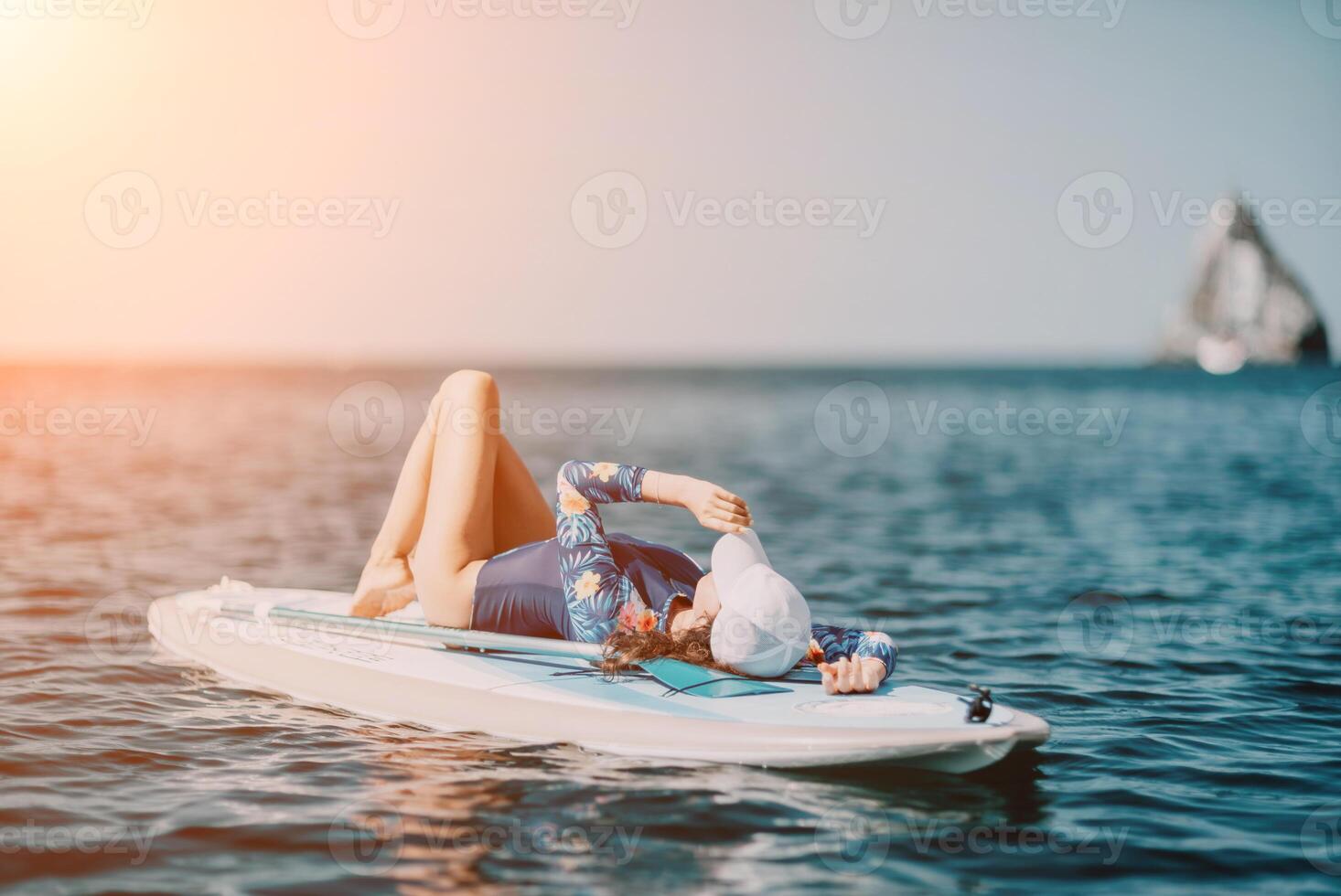 Woman sup yoga. Middle age sporty woman practising yoga pilates on paddle sup surfboard. Female stretching doing workout on sea water. Modern individual female hipster outdoor summer sport activity. photo