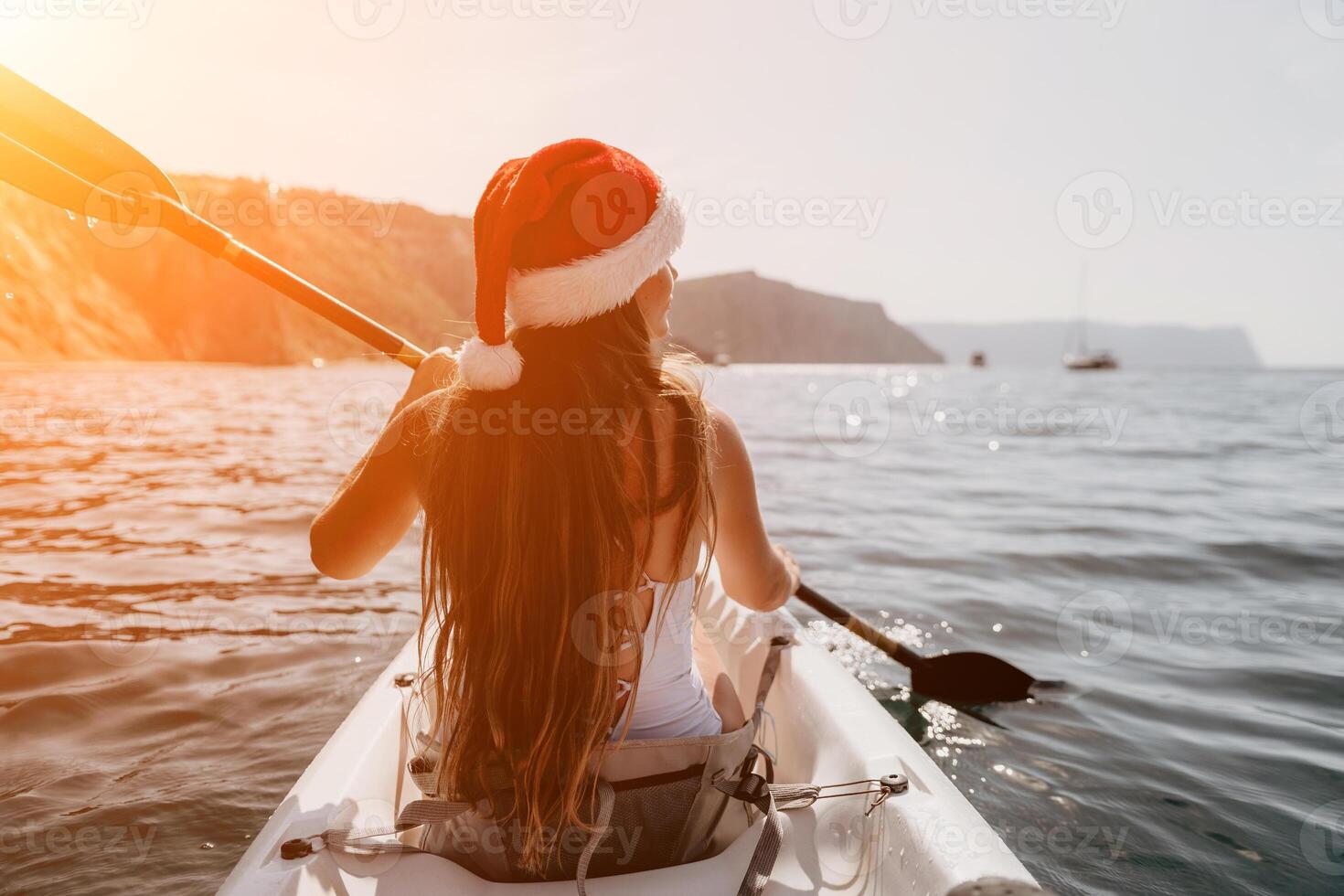 Woman in kayak back view. Happy young woman in Santa hat floating in kayak on calm sea. Summer holiday vacation and cheerful female people relaxing having fun on the boat. photo