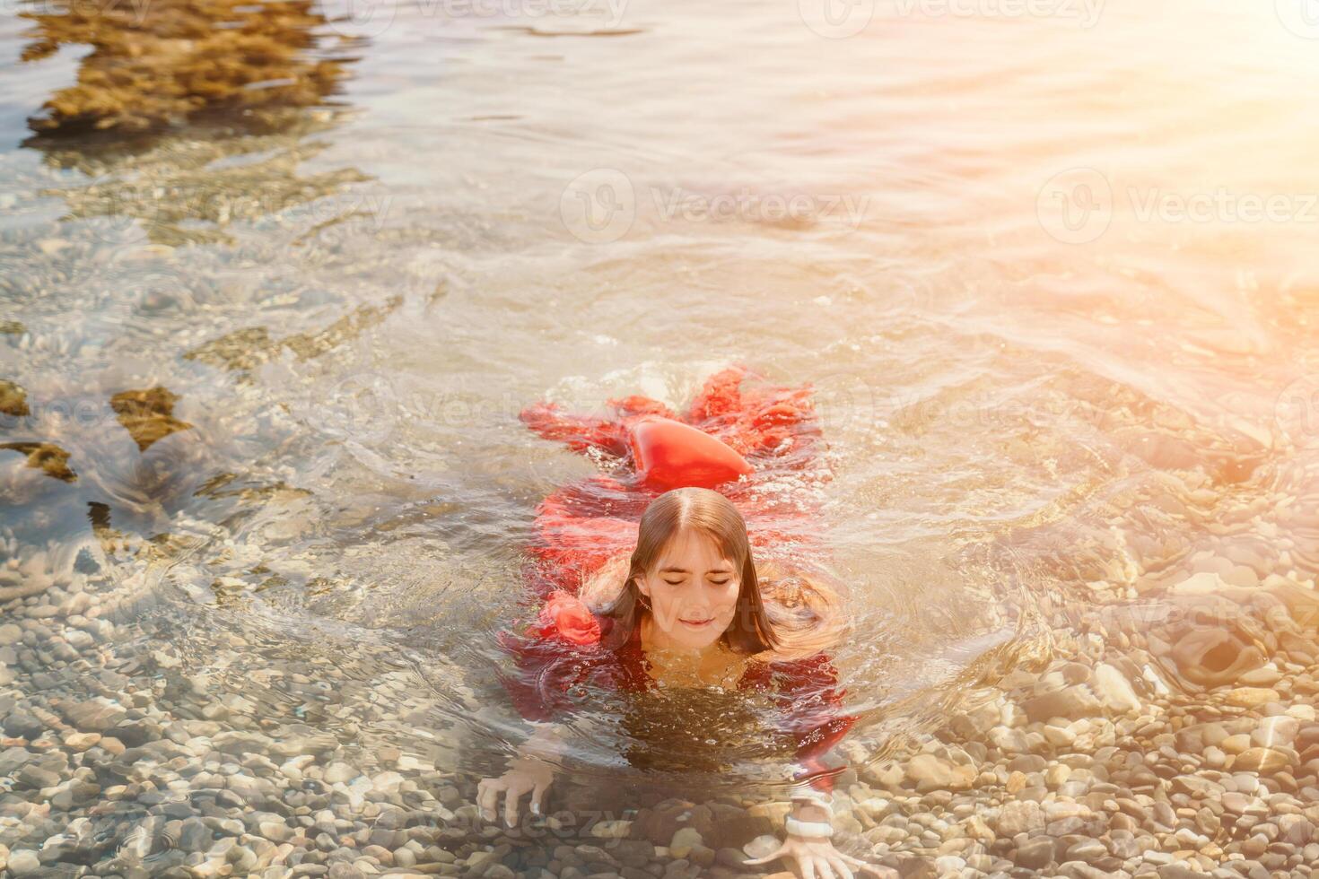 Woman travel sea. Happy tourist in red dress enjoy taking picture outdoors for memories. Woman traveler posing in sea beach, surrounded by volcanic mountains, sharing travel adventure journey photo