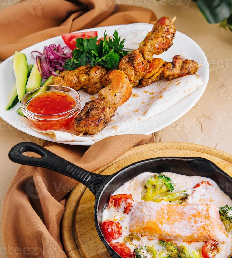 Fried salmon with creamy sauce and pork kebab on a wooden skewer photo