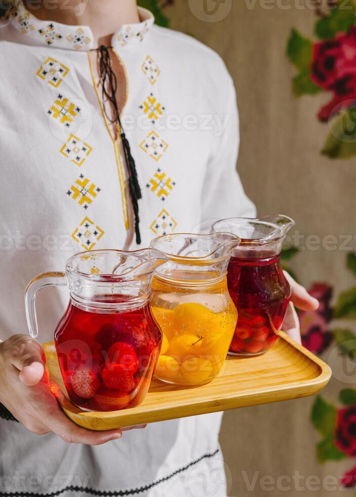 Person presents three pitchers of refreshing fruit-infused water on a wooden tray photo