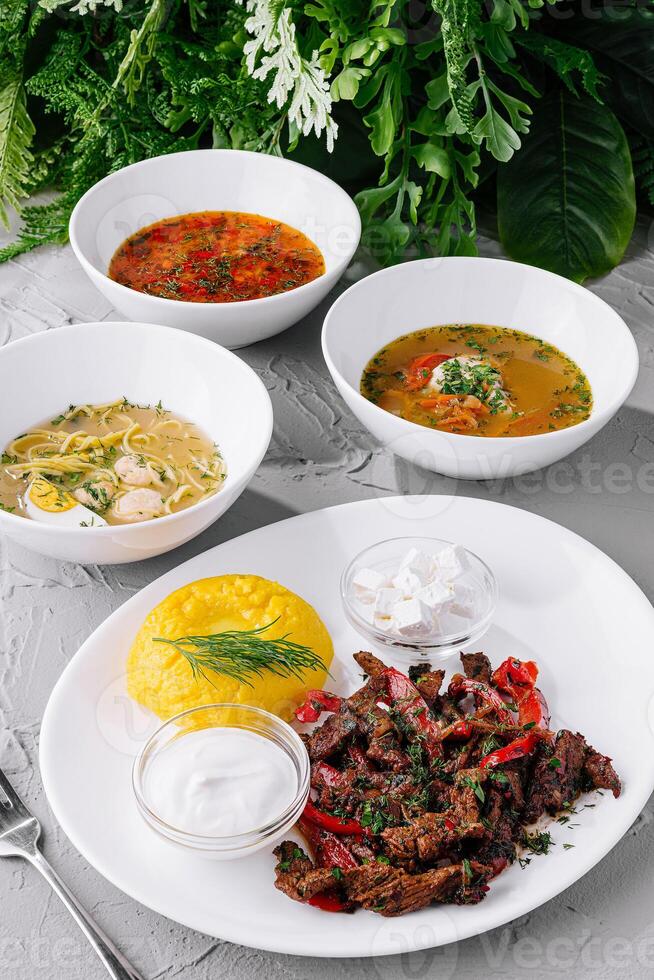 Variety of hearty homemade soups and meat dish on table photo