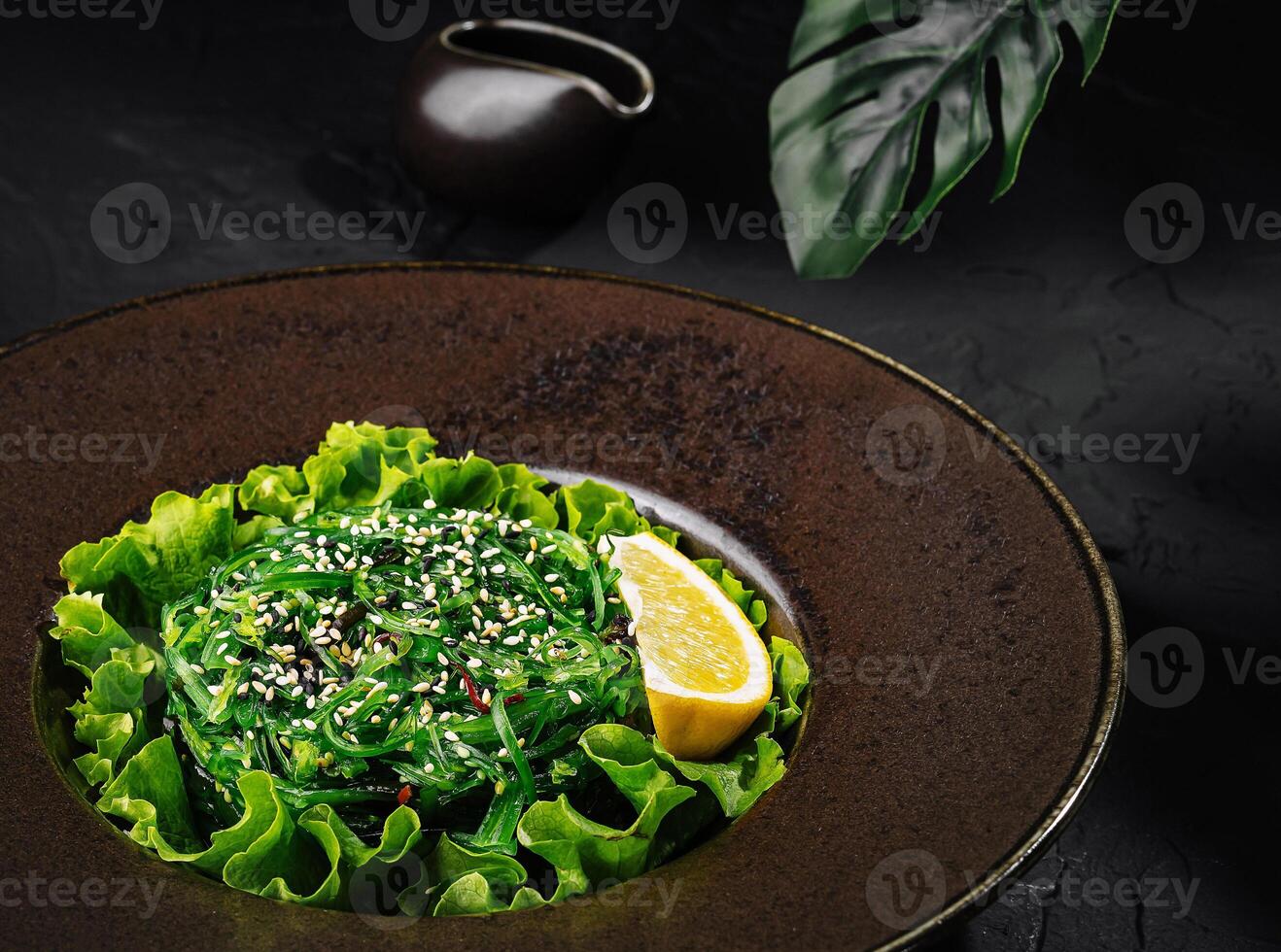 Fresh green seaweed salad with sesame seeds on dark plate photo