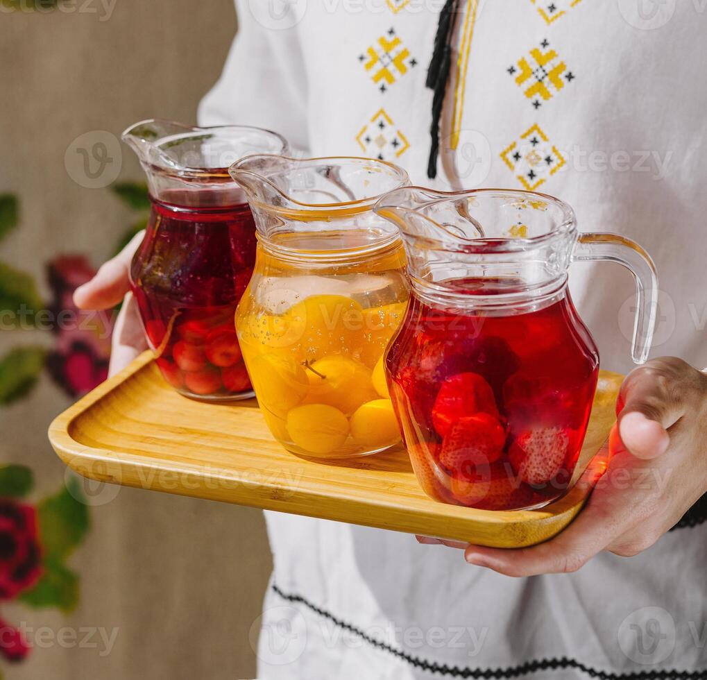 Person presents three pitchers of refreshing fruit-infused water on a wooden tray photo