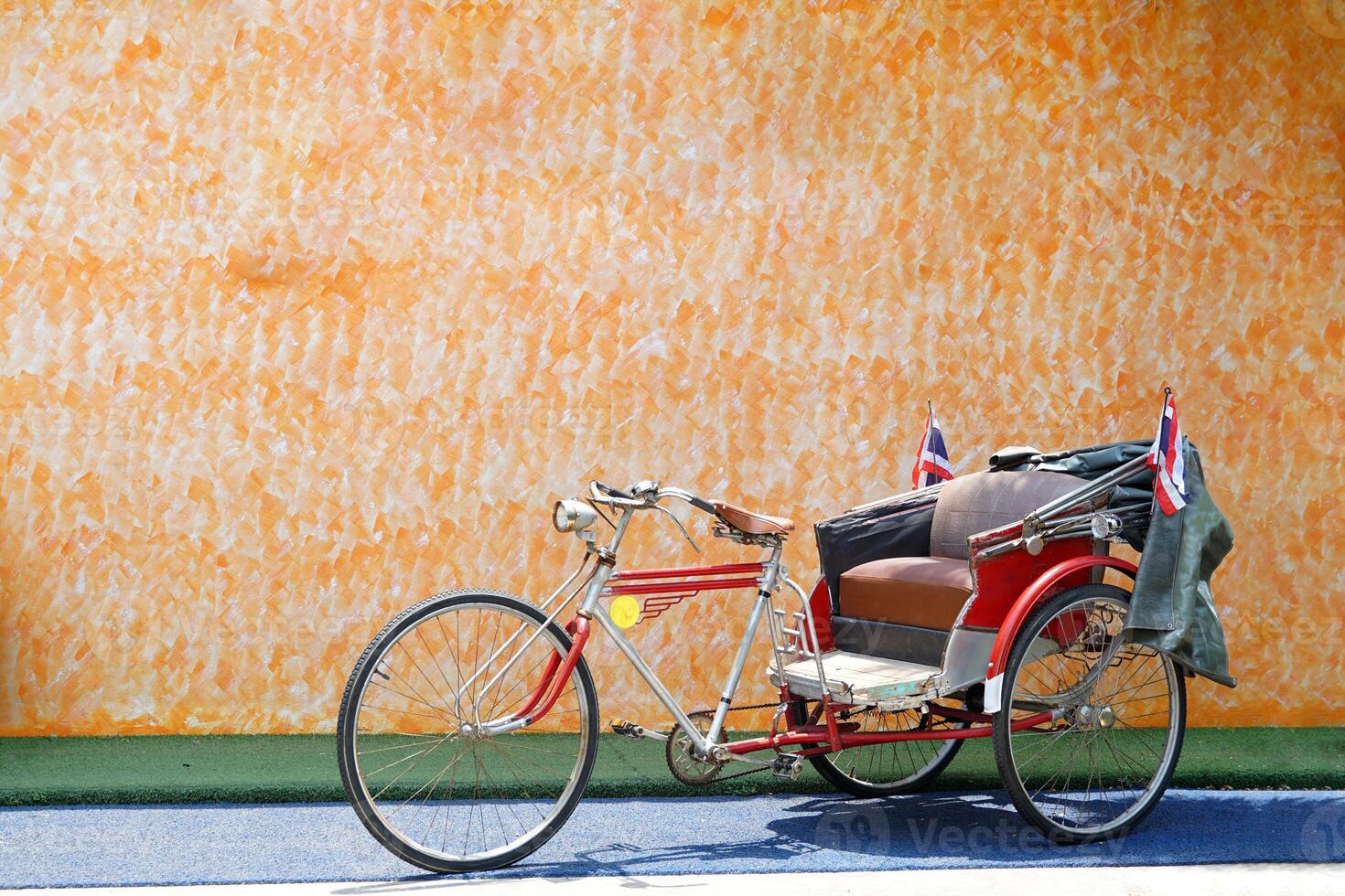 An old tricycle stops as a check-in point at a restaurant with an orange cement wall background. In the past, it was a vehicle that Thai people preferred to use. Currently serving tourists. photo