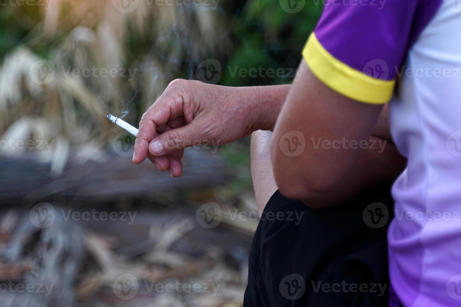 Asian man's hand holds a lit cigarette and sits alone smoking in the smoking corner of his house. photo