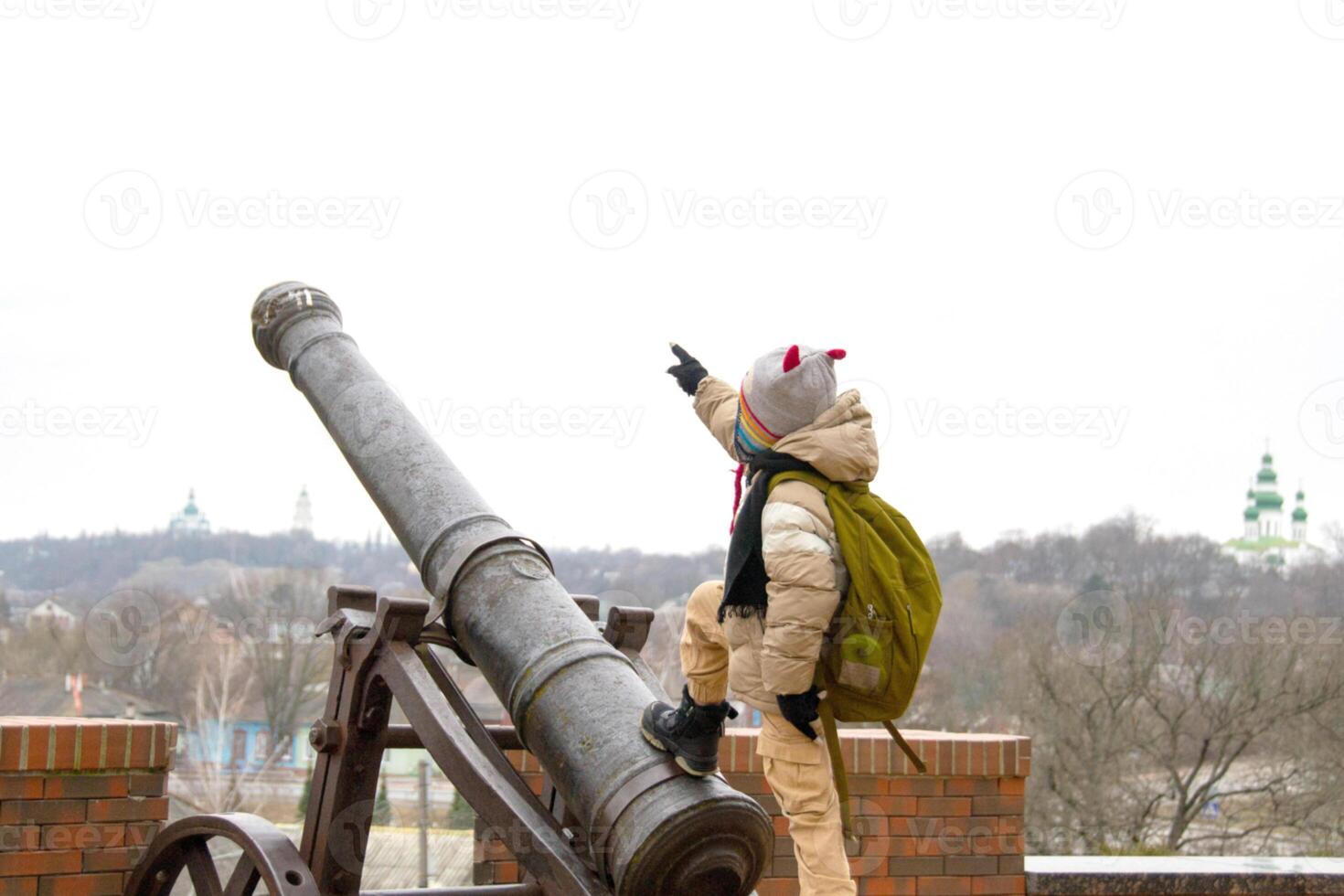 a handsome boy stands against the background of an ancient cannon photo
