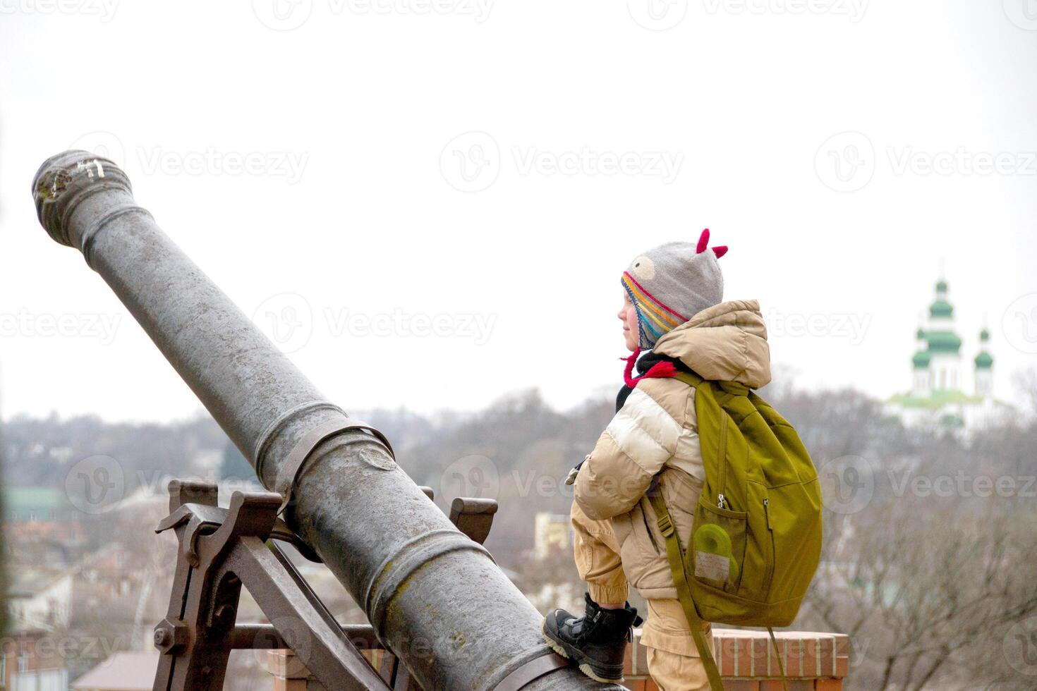 a handsome boy stands against the background of an ancient cannon photo