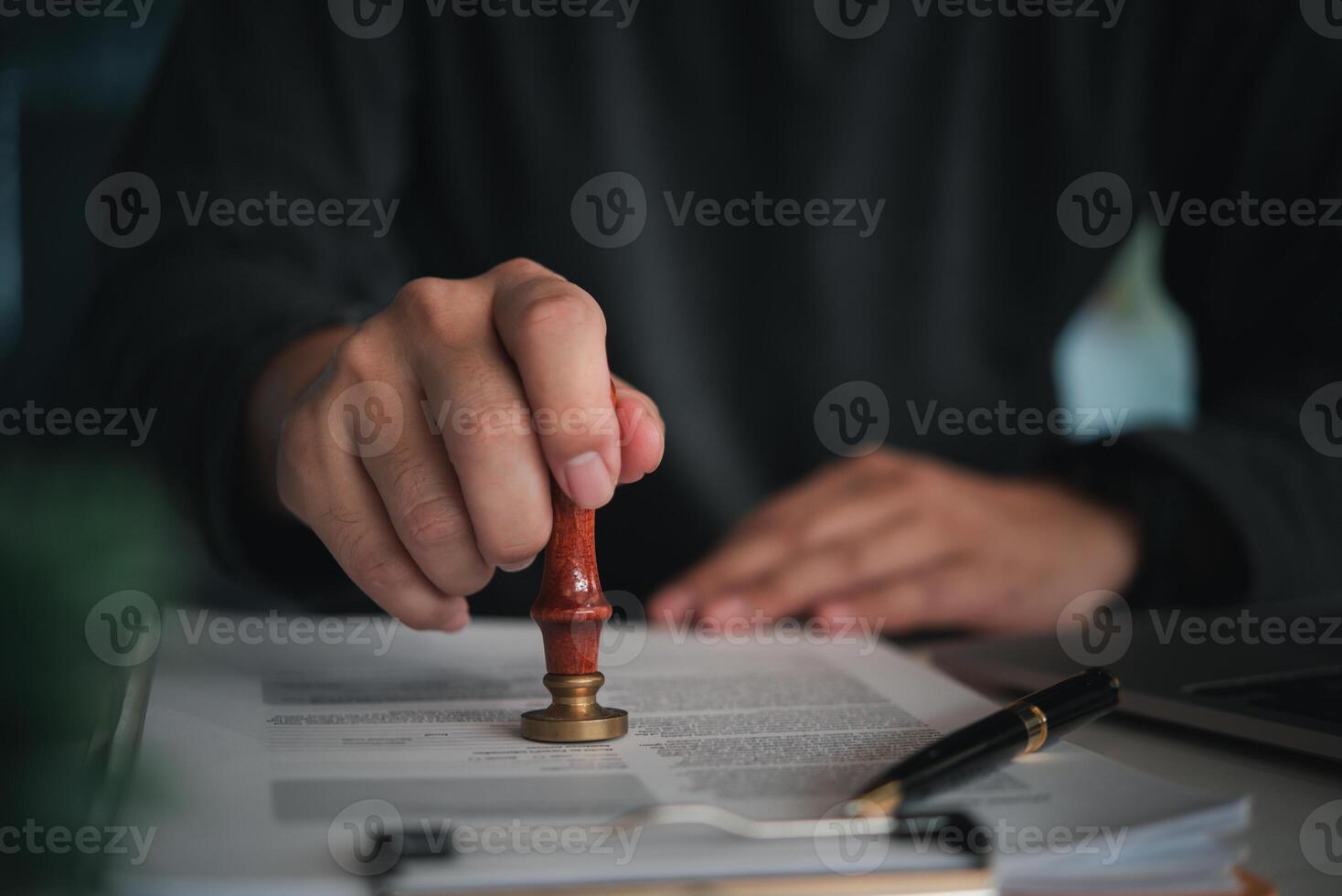 Focused individual placing a seal on an official document with red wax stamp in a professional setting photo