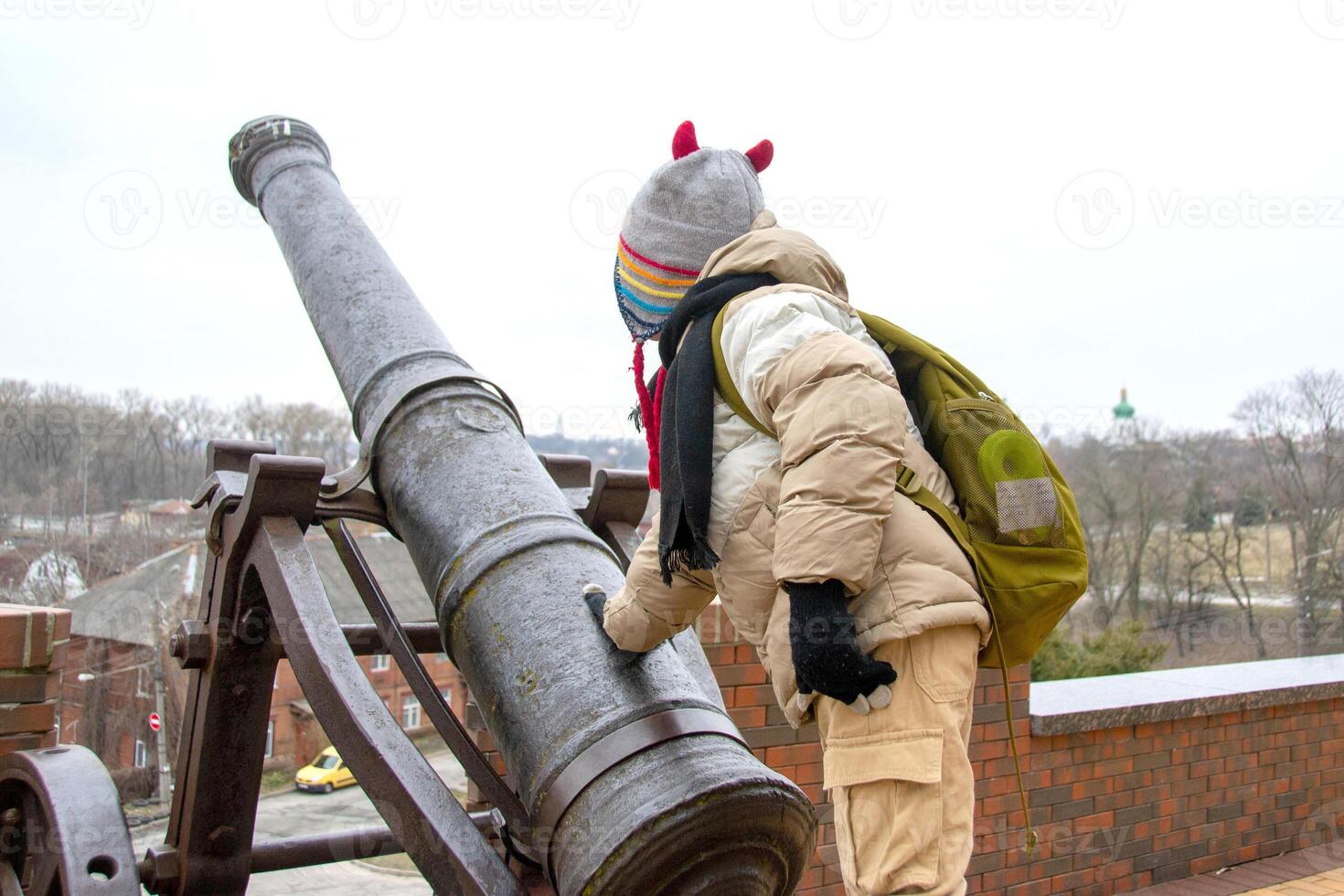 a handsome boy stands against the background of an ancient cannon photo