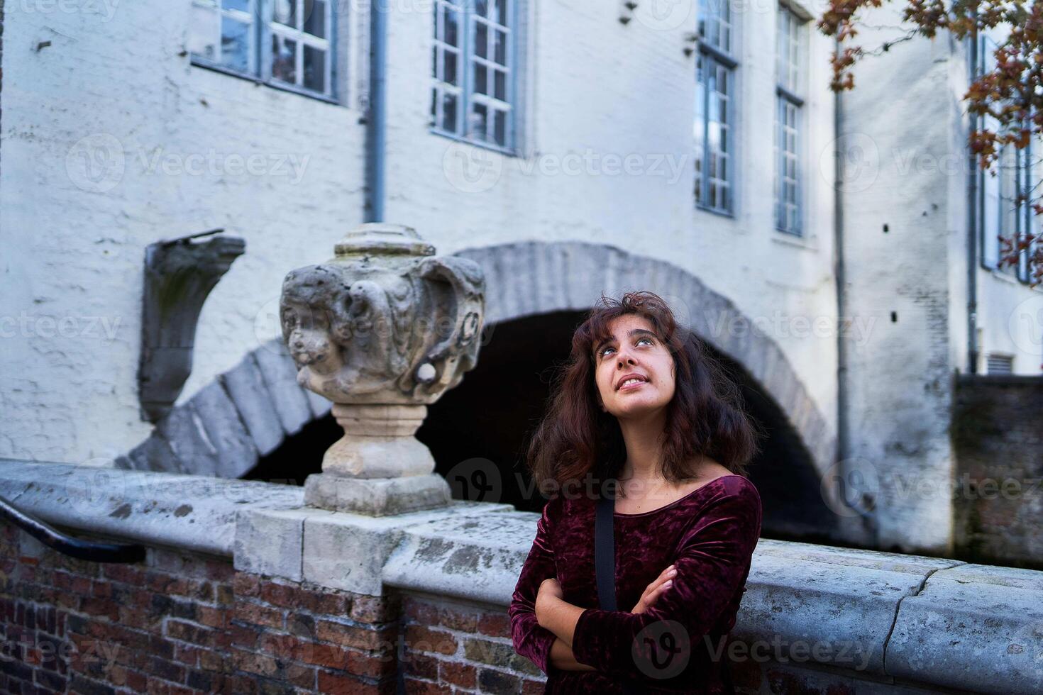 a girl in a red corduroy dress with an open back walks through the streets of Bruges on an autumn day photo