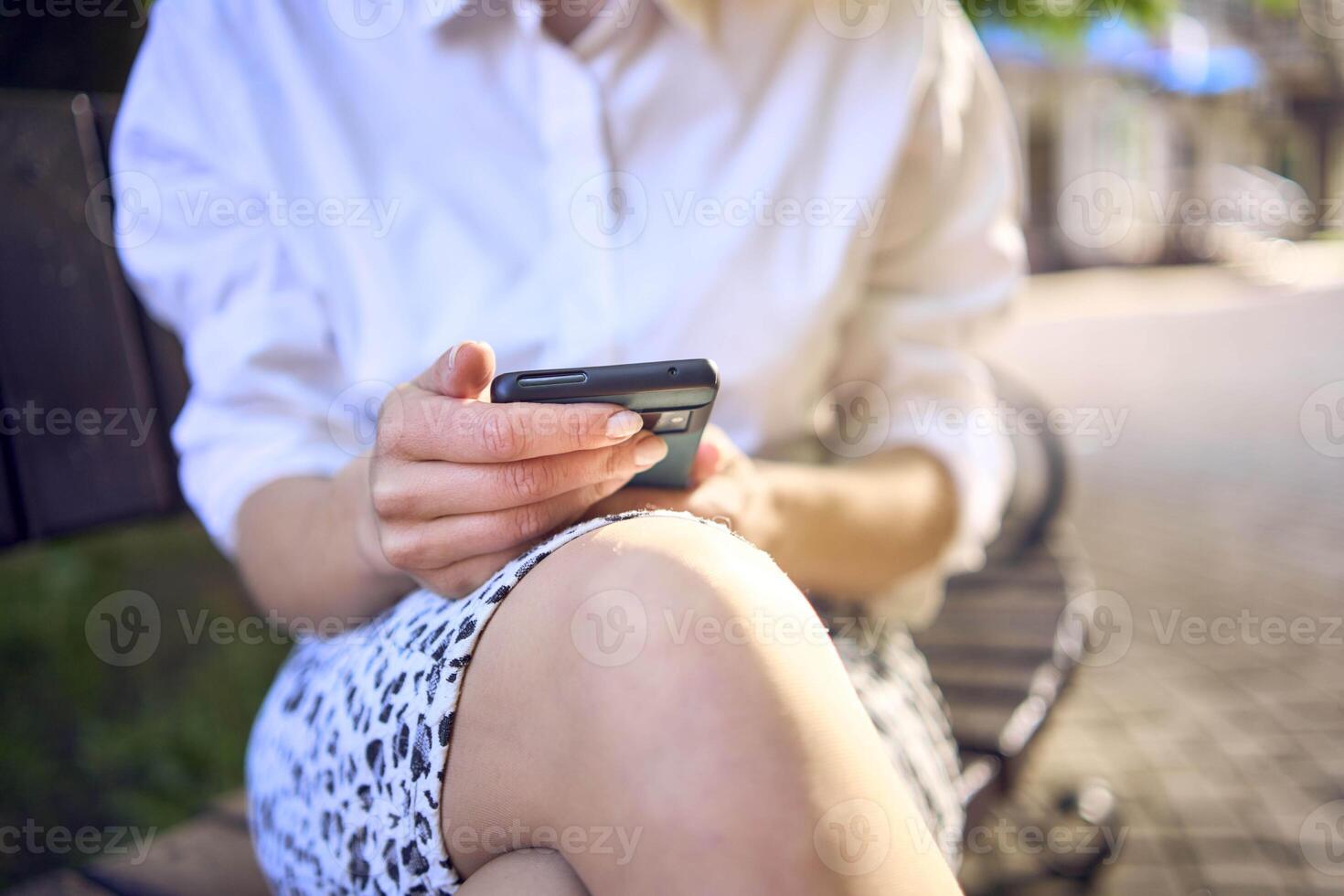a beautiful middle age woman in 70s, 80s style clothes is looking at her smartphone on a bench photo