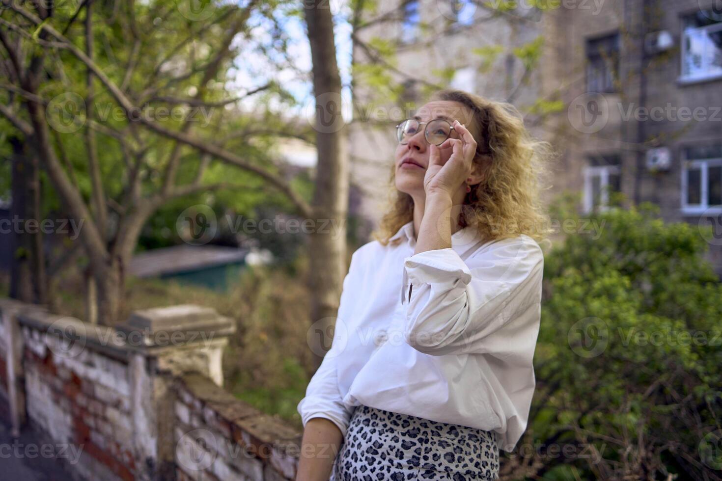 middle age woman in 70s, 80s style clothes with a coffee stain on her blouse in front of gray houses of the 70s photo