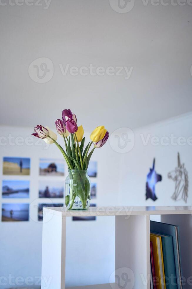 bouquet of multicolored tulips in a transparent jar in the interior photo