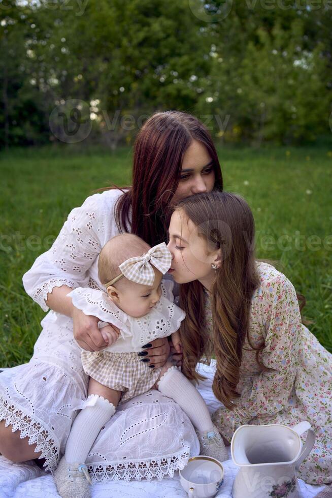 sisters of different ages hug each other tenderly on a picnic in the garden photo