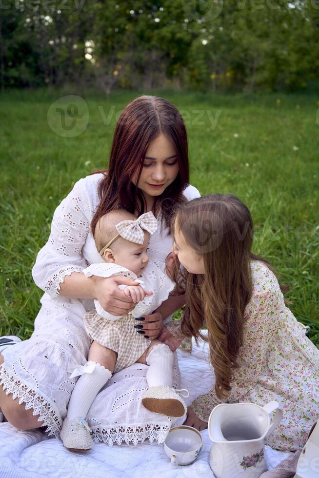 sisters of different ages hug each other tenderly on a picnic in the garden photo