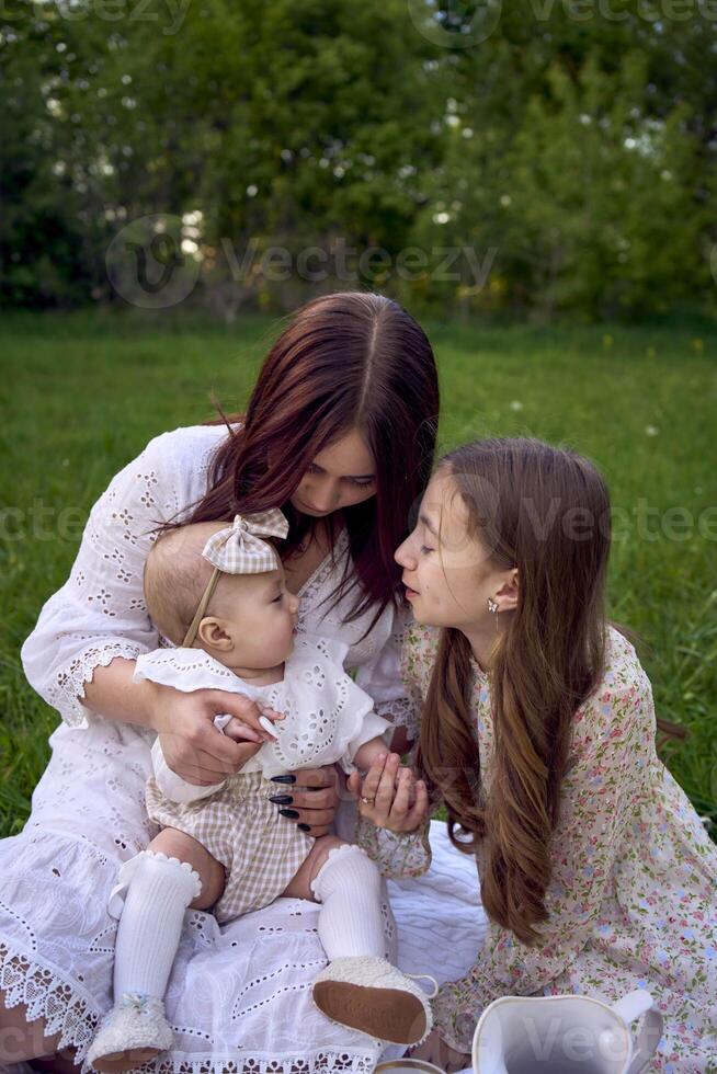 sisters of different ages hug each other tenderly on a picnic in the garden photo