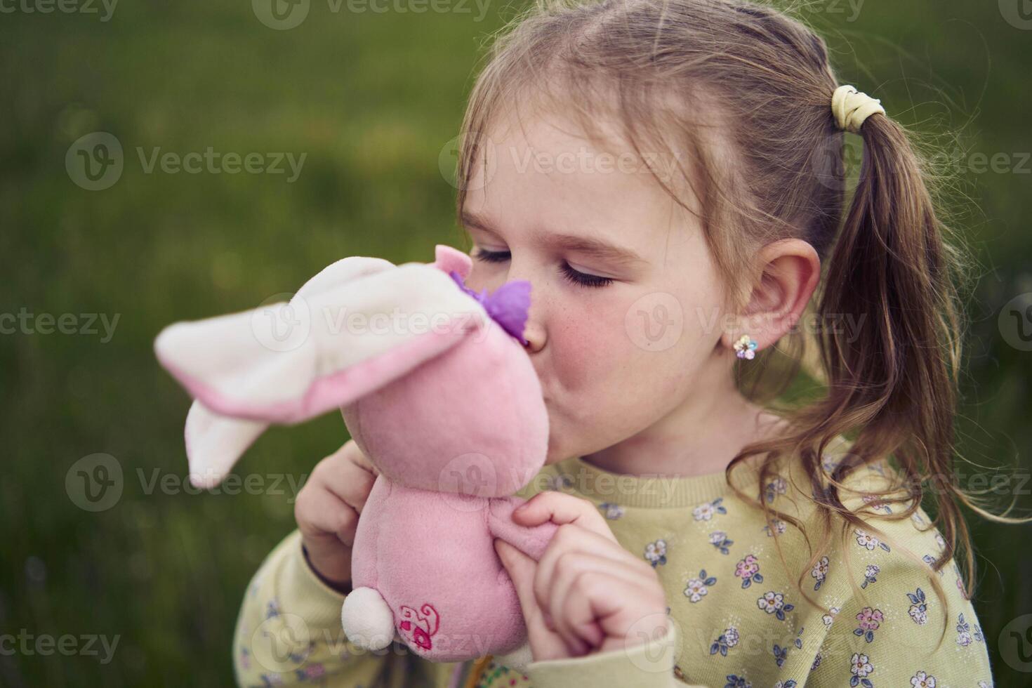 a beautiful blond girl with her toy bunny is playing in the field photo