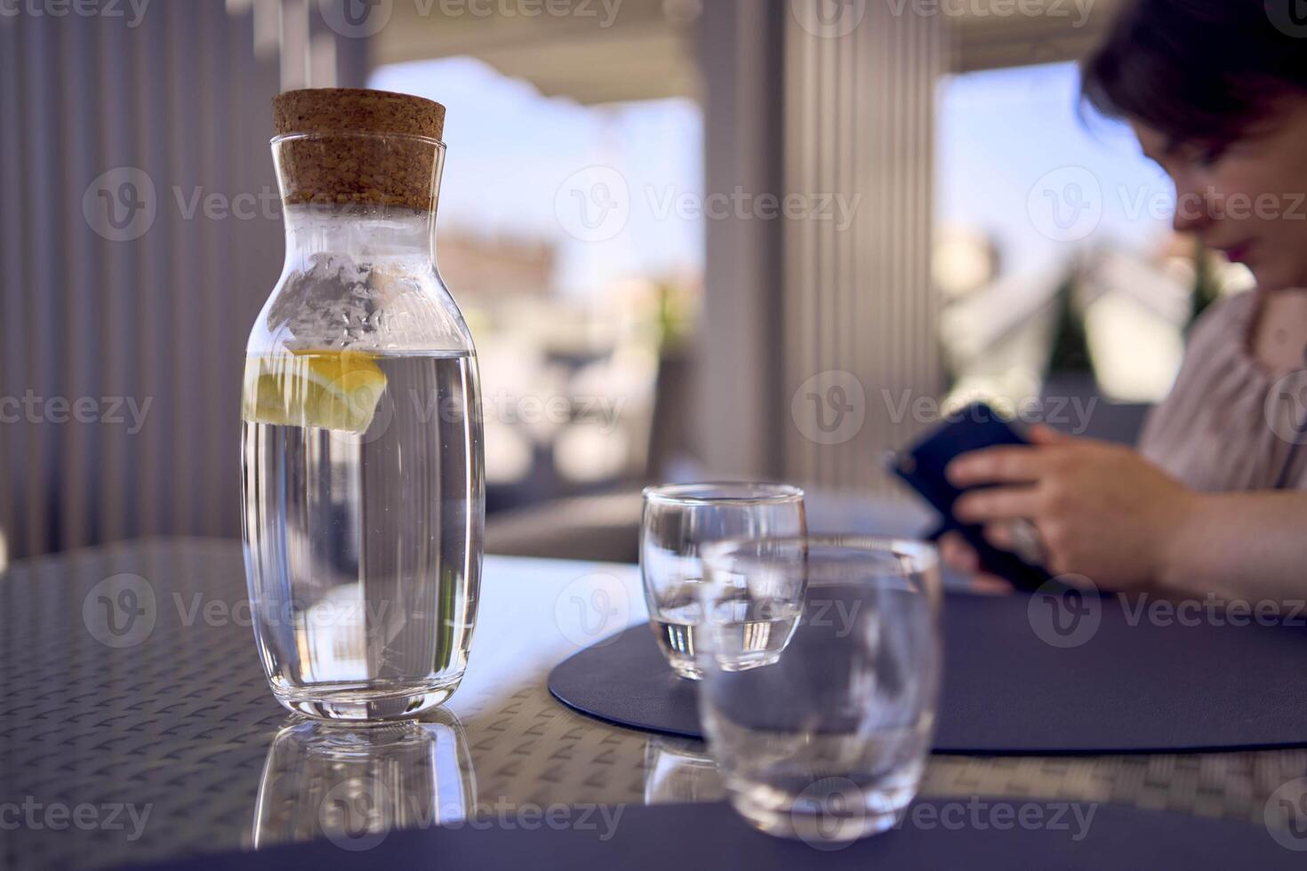 plus size woman in peach fuzz dress chooses a dish in a restaurant via QR code in smartphone, water with lemon and glasses in front of her photo