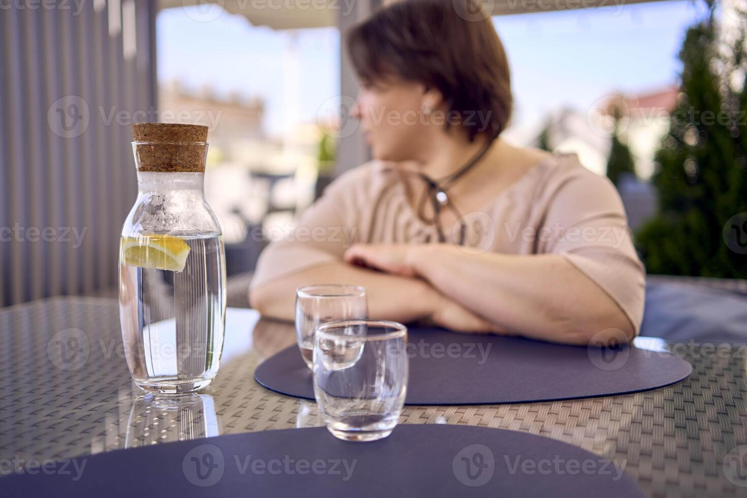plus size woman in peach fuzz dress chooses a dish in a restaurant via QR code in smartphone, water with lemon and glasses in front of her photo