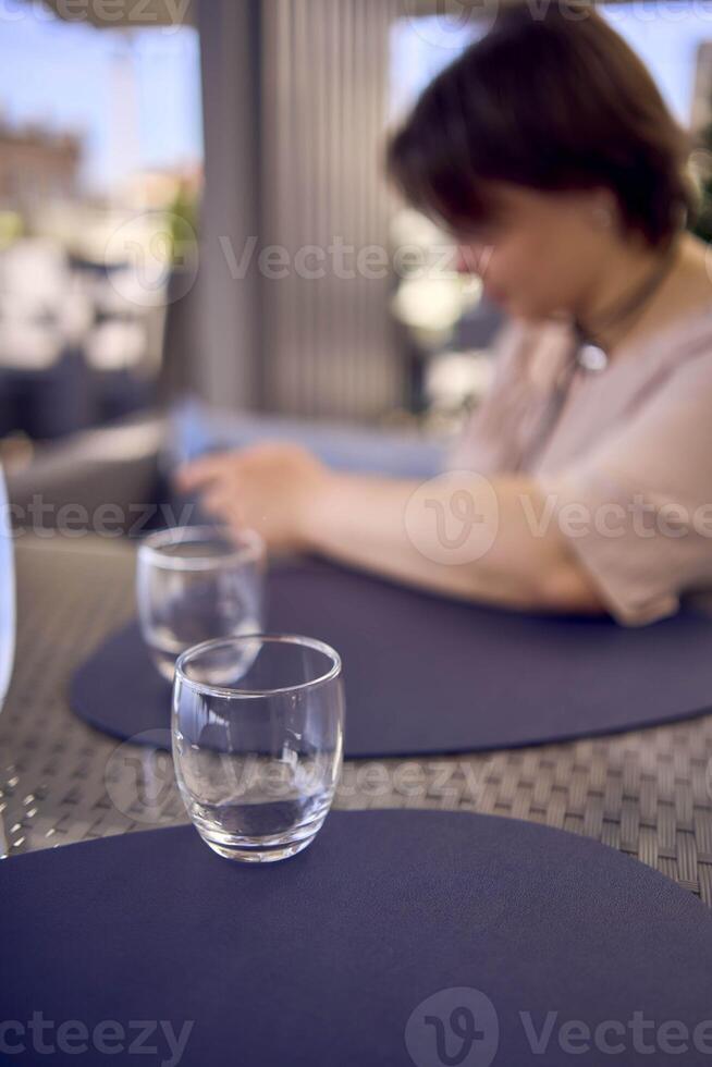 plus size woman in peach fuzz dress chooses a dish in a restaurant via QR code in smartphone, water with lemon and glasses in front of her photo