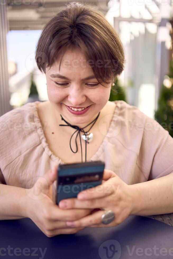 plus size woman in peach fuzz dress chooses a dish in a restaurant via QR code in smartphone, water with lemon and glasses in front of her photo