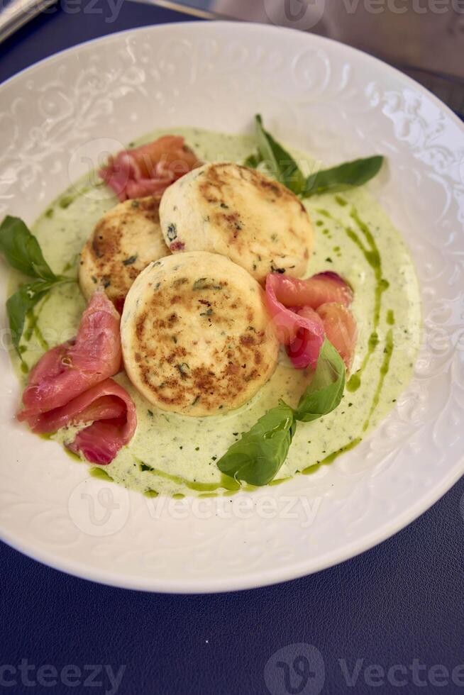 medium sized woman in peach fuzz dress eating cottage cheese pancakes with salmon and spinach in modern restaurant photo