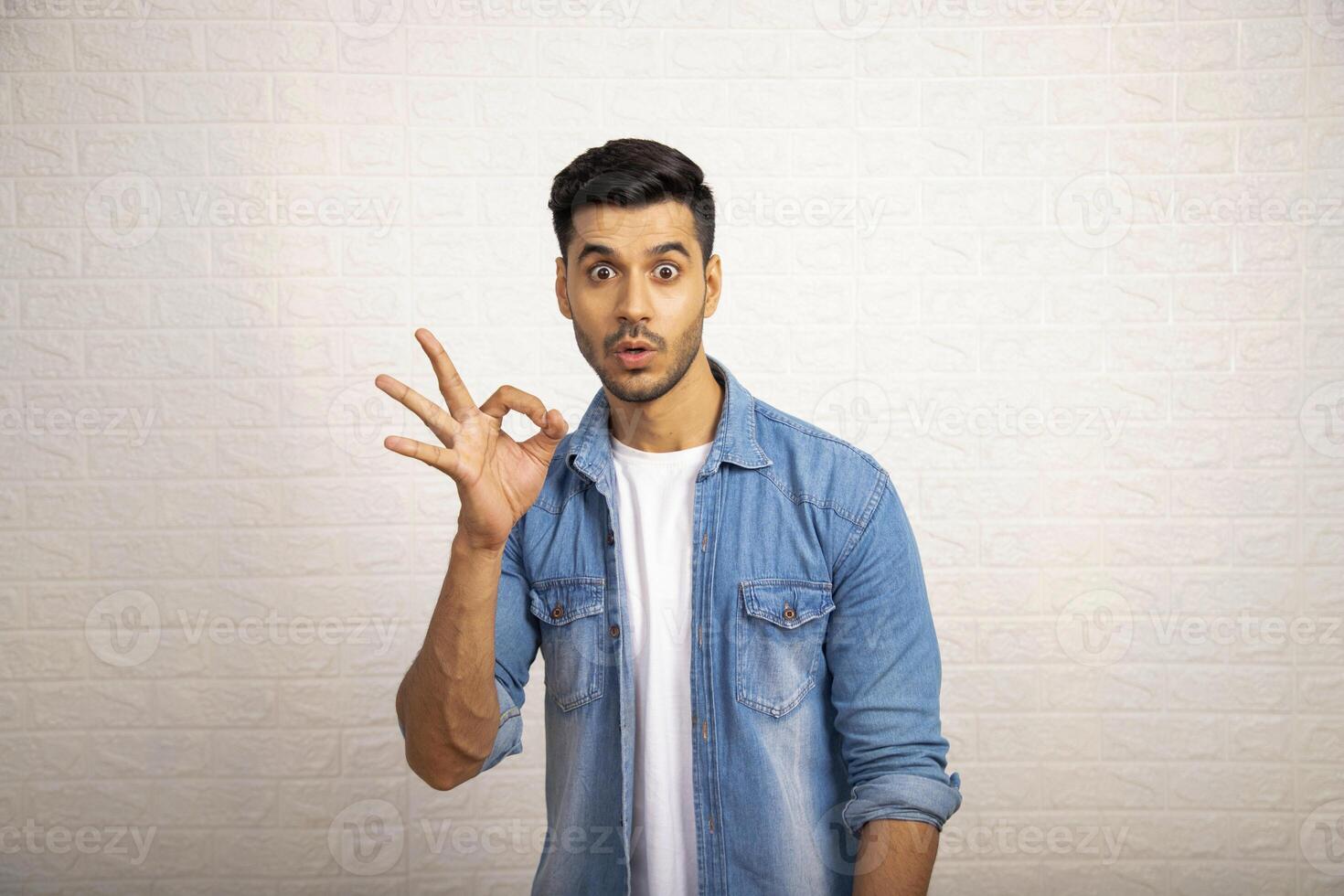 Asian Man With Surprised Face Expression Making Super Ok Gesture With Hand photo