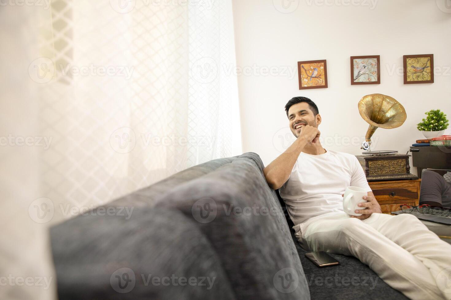 Man In White Tshirt Smiling Holding White Mug In Hand While Sitting On Sofa photo