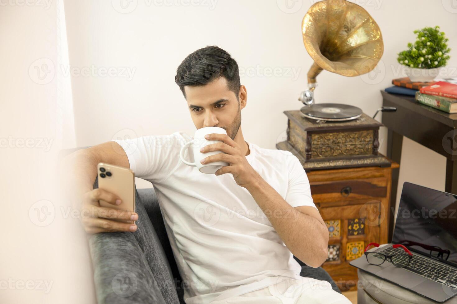 Man Using Cellphone While Drinking Coffee Sitting On Sofa photo