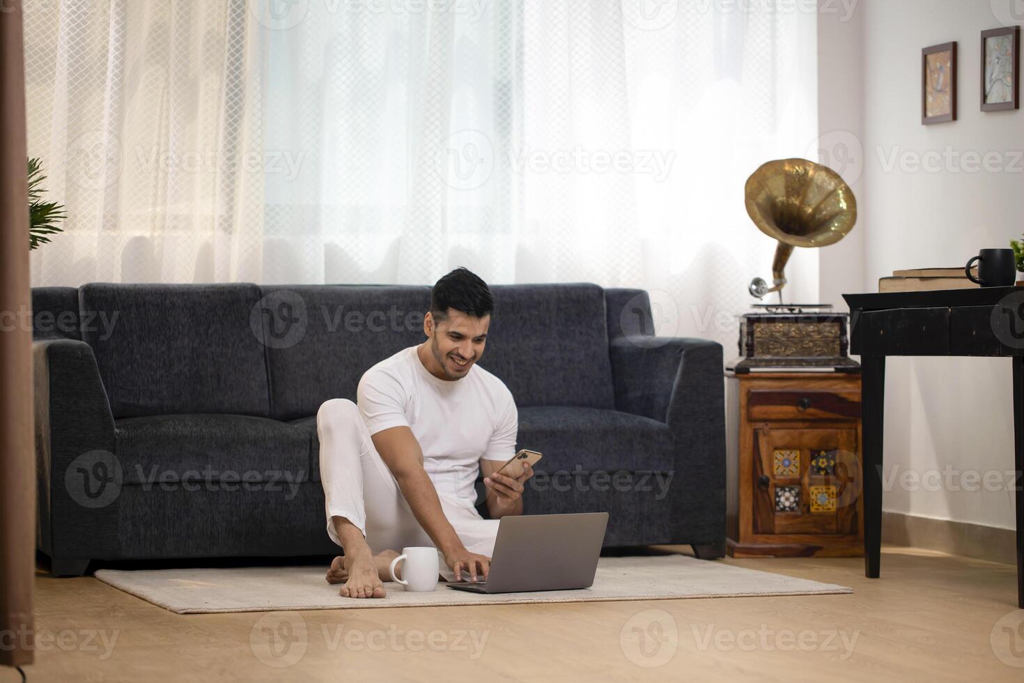 Young Man Working On Laptop And Holding Mobile In Another Hand photo