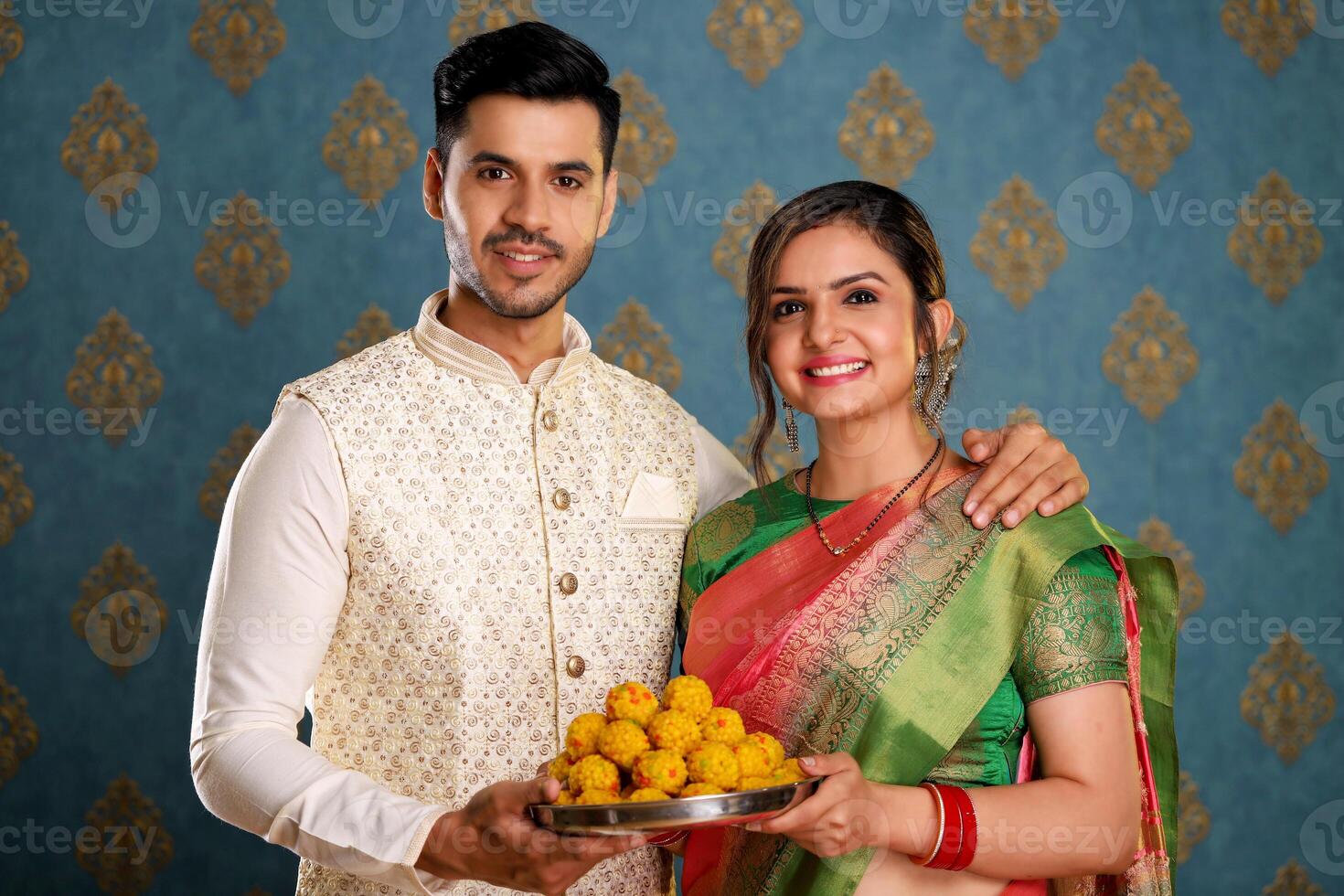 Photo of Romantic Couple In Traditional Indian Outfits Holding Laddoo Plate