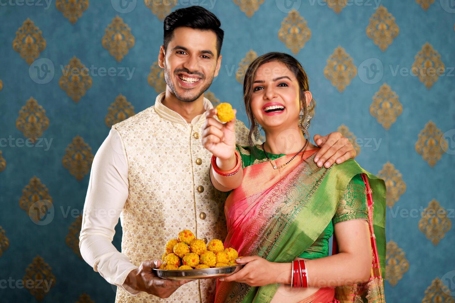 Image Of A Traditional Couple In Traditional Indian Outfits Holding A Plate Of Laddu In Their Hands And Showing A Laddu To The Camera photo