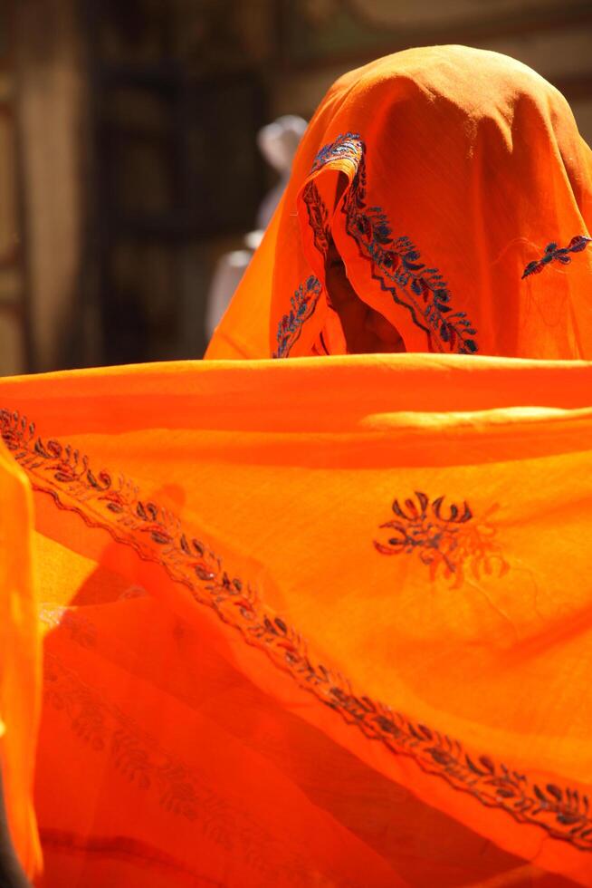 indian woman hiding face behind orange clothes, sari photo