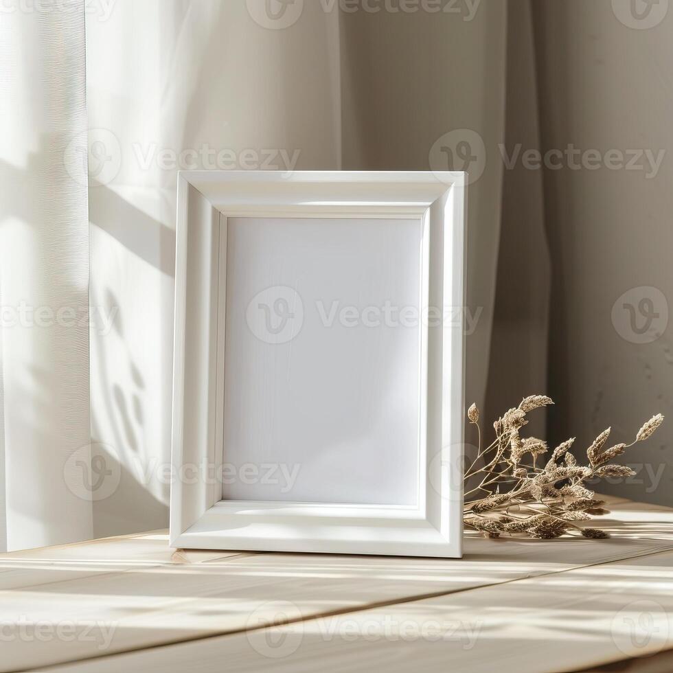 An empty white picture frame sits on a wooden table in front of a sheer white curtain. photo